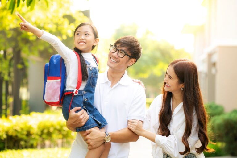 Family walking to school — two parents and the dad is holding their daughter who has a backpack on