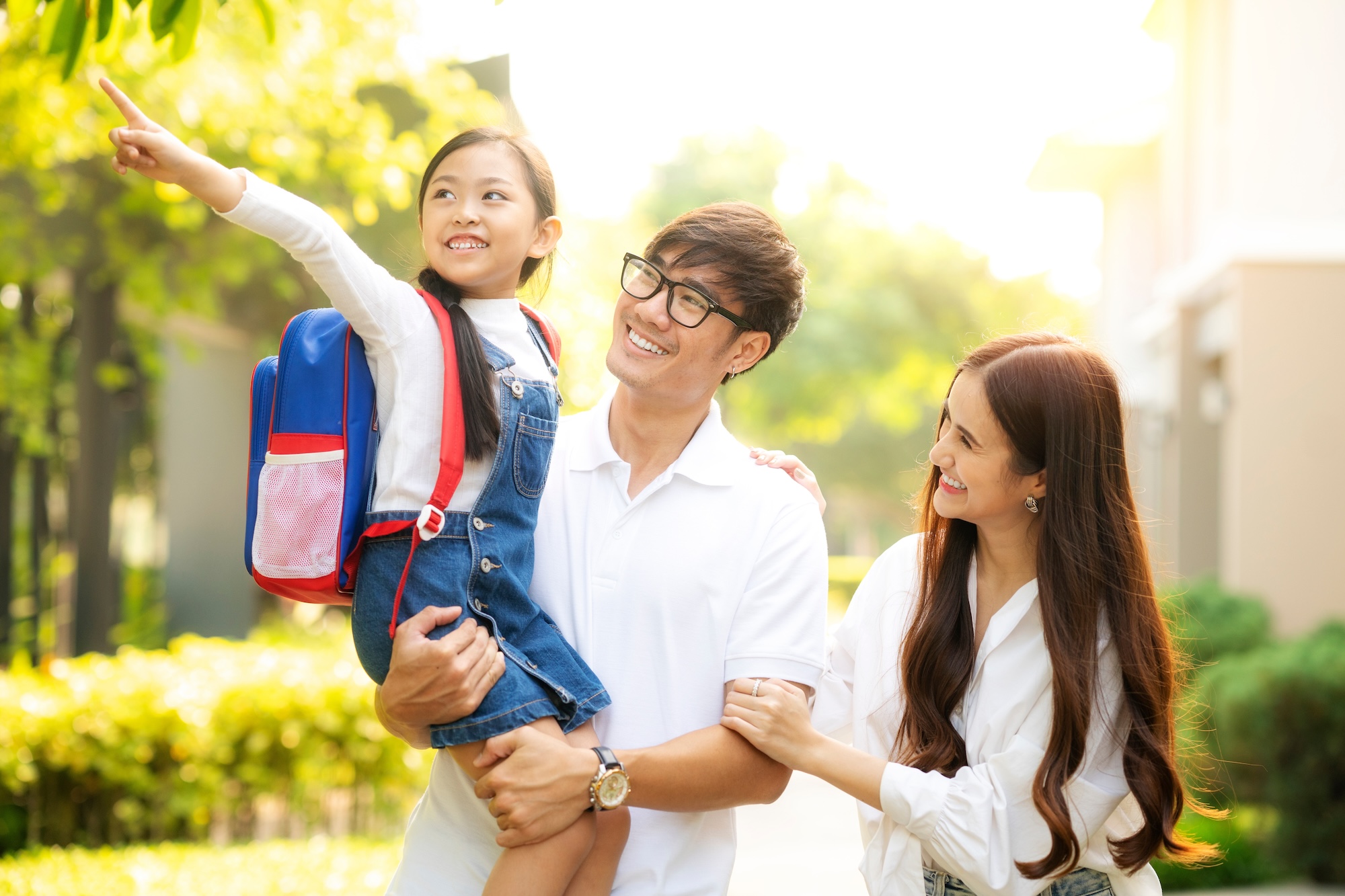 Family walking to school — two parents and the dad is holding their daughter who has a backpack on