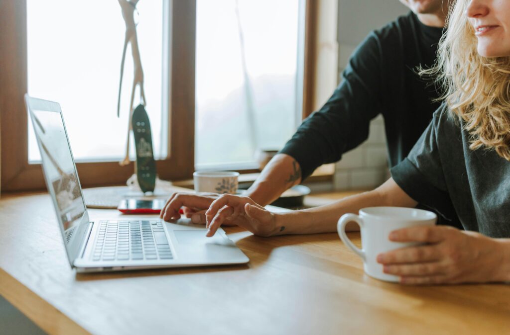 "Two people using a laptop together while having coffee."