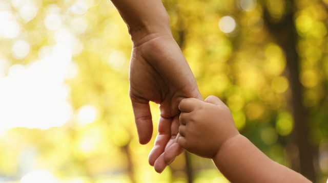 Daughter holding mother's hand outdoors, closeup. Happy family
